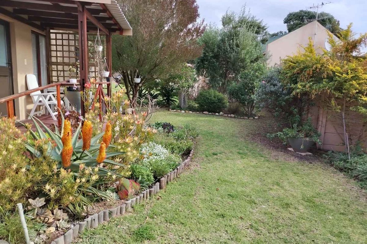 A well-maintained rear garden featuring a timber deck with a pergola, established landscaping, and a lawn area.