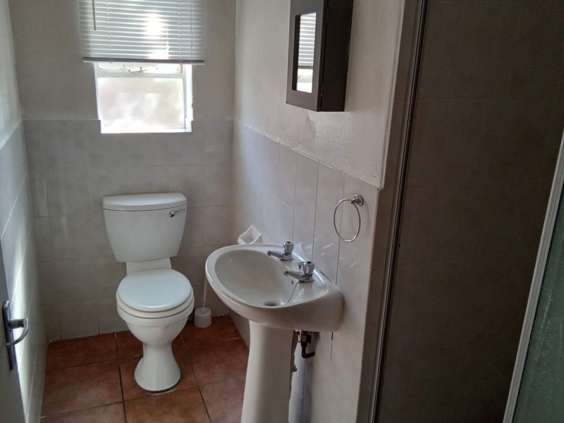 A functional bathroom featuring a pedestal basin, toilet, and shower enclosure with tiled finishes, requiring cosmetic updates to improve its overall condition.