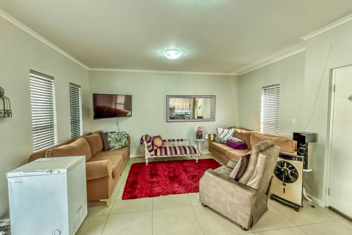A spacious living room featuring neutral tiled flooring, large windows with fitted blinds, and recessed ceiling lighting.