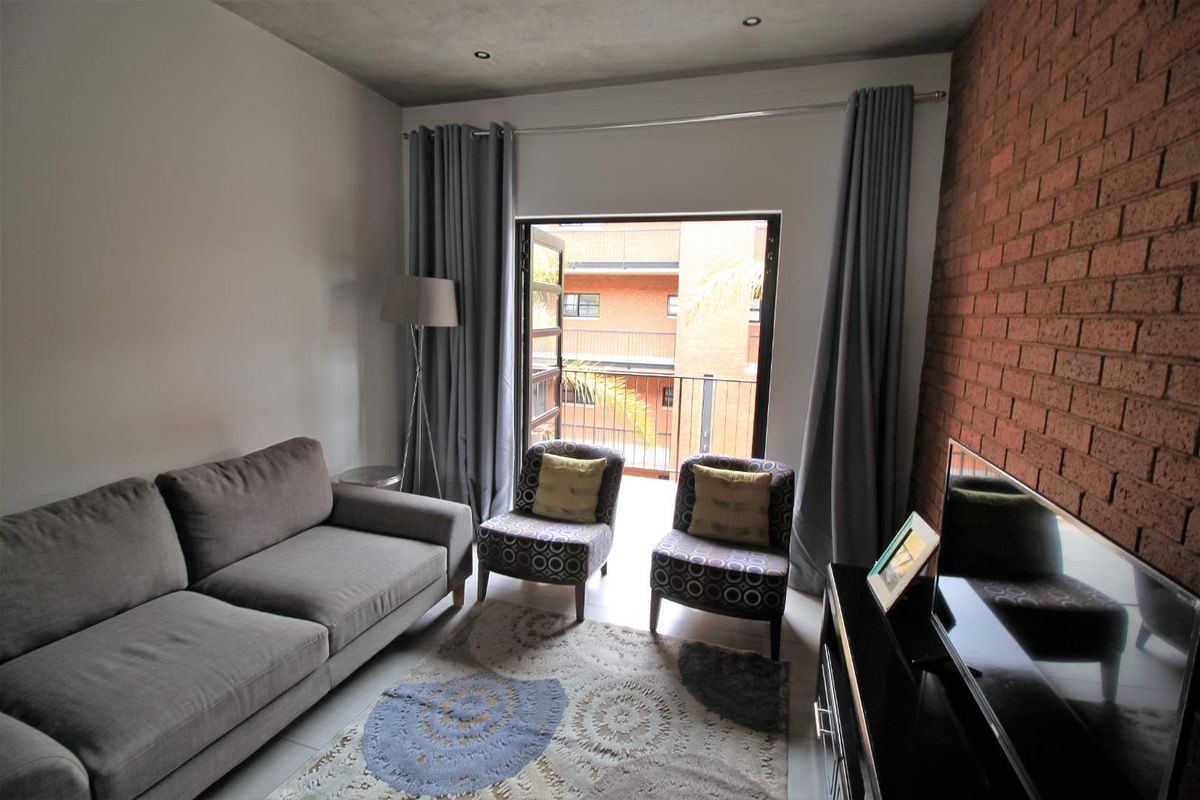 A modern living room featuring an exposed brick accent wall, concrete ceiling, and direct access to a private balcony.