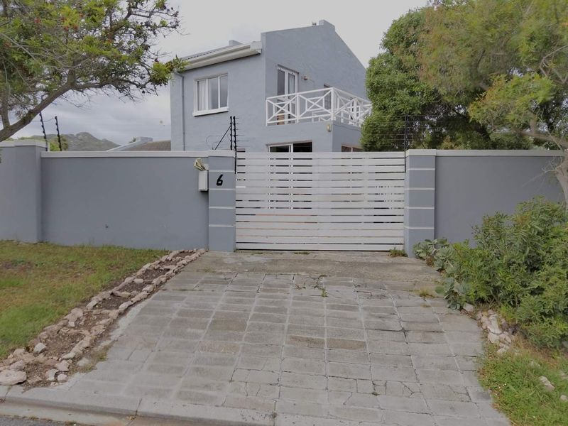 Front view of a two-story house featuring a paved driveway, secure boundary wall with electric fencing, and an upper-level balcony.