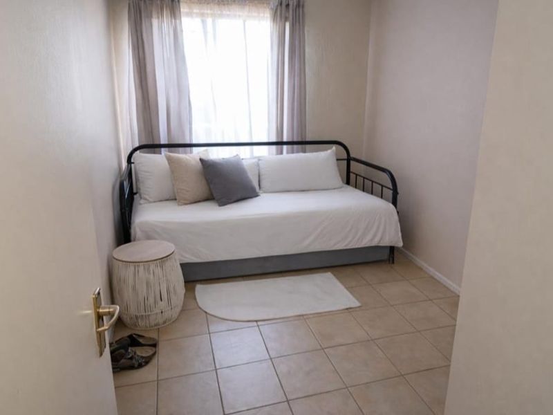 A compact bedroom featuring neutral tiled flooring and a window with installed curtain rails, providing a functional space for a single bed.