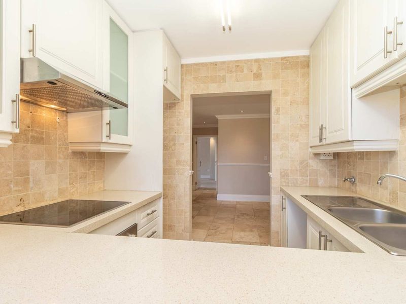 A clean, functional kitchen featuring stone countertops, built-in cabinetry, an electric hob with extractor fan, and a double stainless steel sink with tiled backsplash.