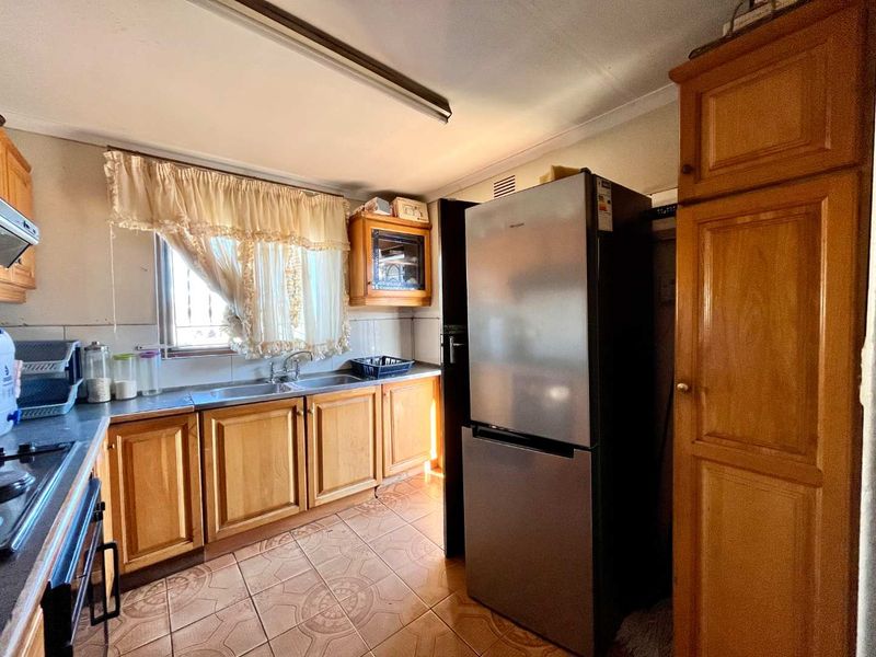 A functional kitchen featuring wooden cabinetry, tiled flooring, and a double basin sink, offering potential for a modern renovation.