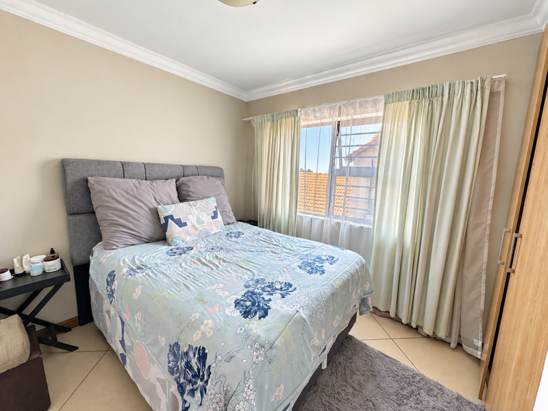 A well-maintained bedroom featuring tiled flooring, built-in wardrobe storage, and natural light through a window with security bars.