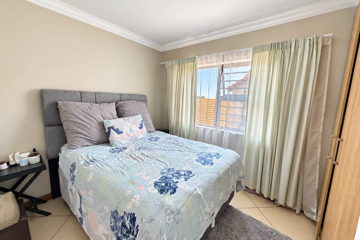 A well-maintained bedroom featuring tiled flooring, built-in wardrobe storage, and natural light through a window with security bars.