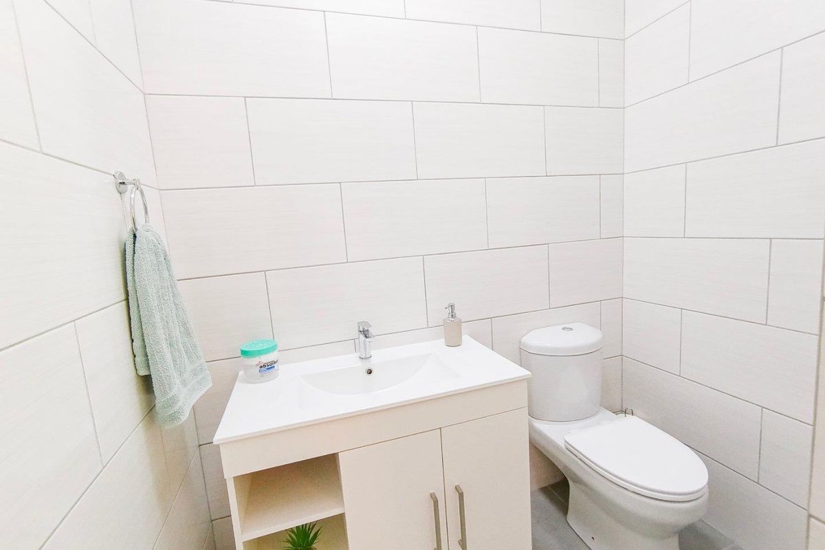 A modern, clean bathroom featuring floor-to-ceiling white subway-style wall tiles, a contemporary vanity unit with integrated basin, and a standard toilet.