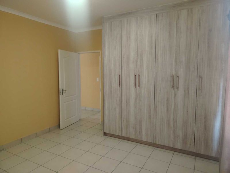 A clean, empty bedroom featuring light-toned built-in cupboards and neutral tiled flooring, offering a versatile space ready for personalization.