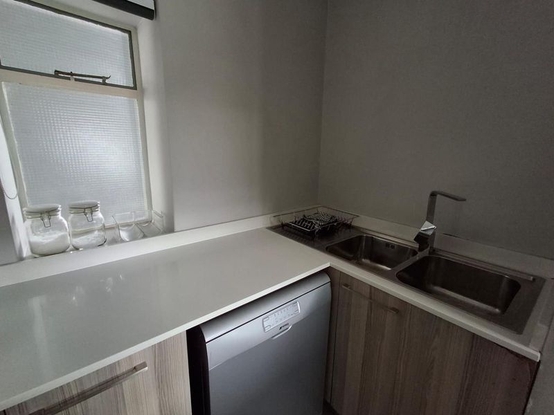 A functional scullery area featuring a double stainless steel sink, stone countertops, and modern laminate cabinetry with an integrated dishwasher.