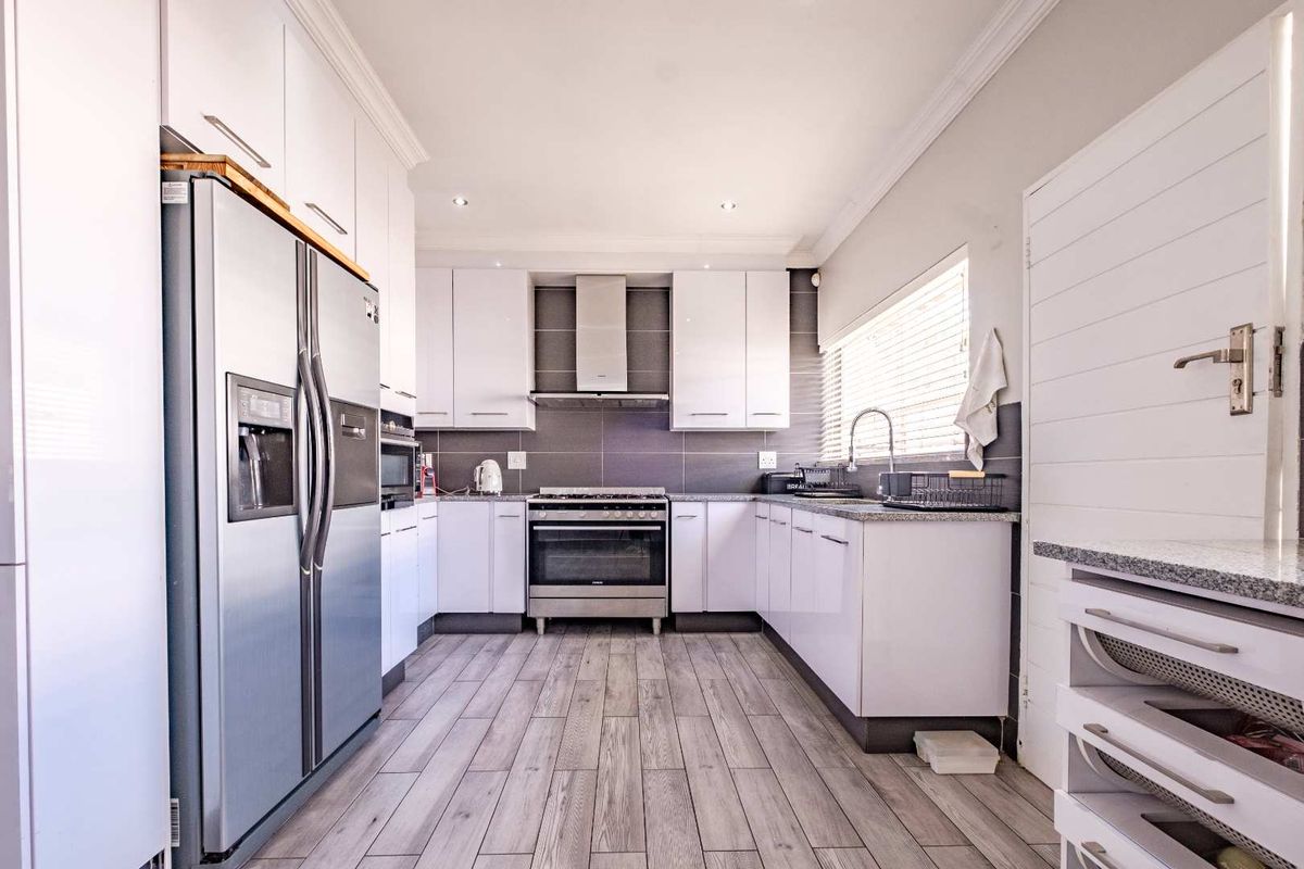 Modern kitchen featuring white cabinetry, granite countertops, stainless steel gas stove, extractor fan, and wood-look tiled flooring.