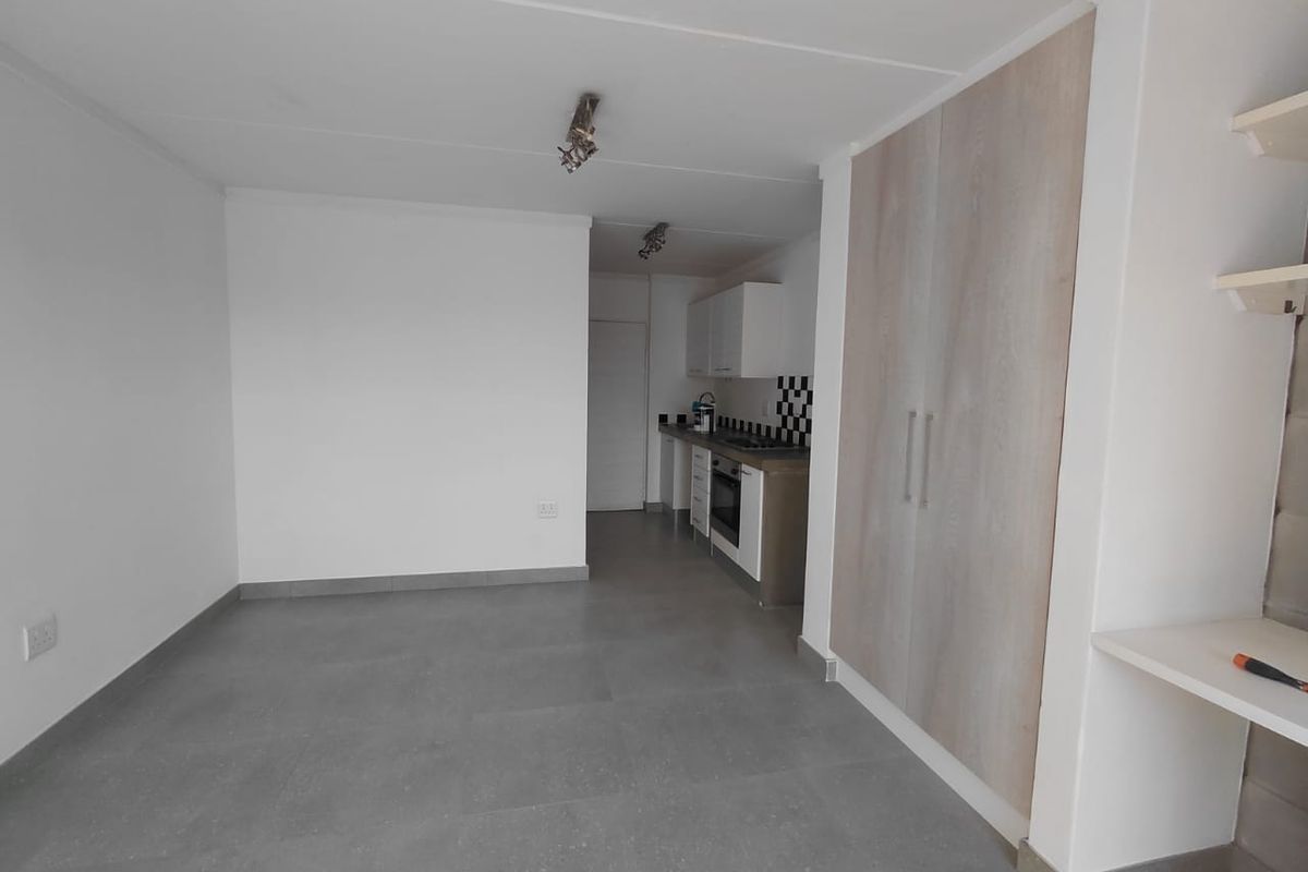 Open plan living area featuring tiled flooring, built-in cabinetry, and a compact kitchen with integrated oven and hob.