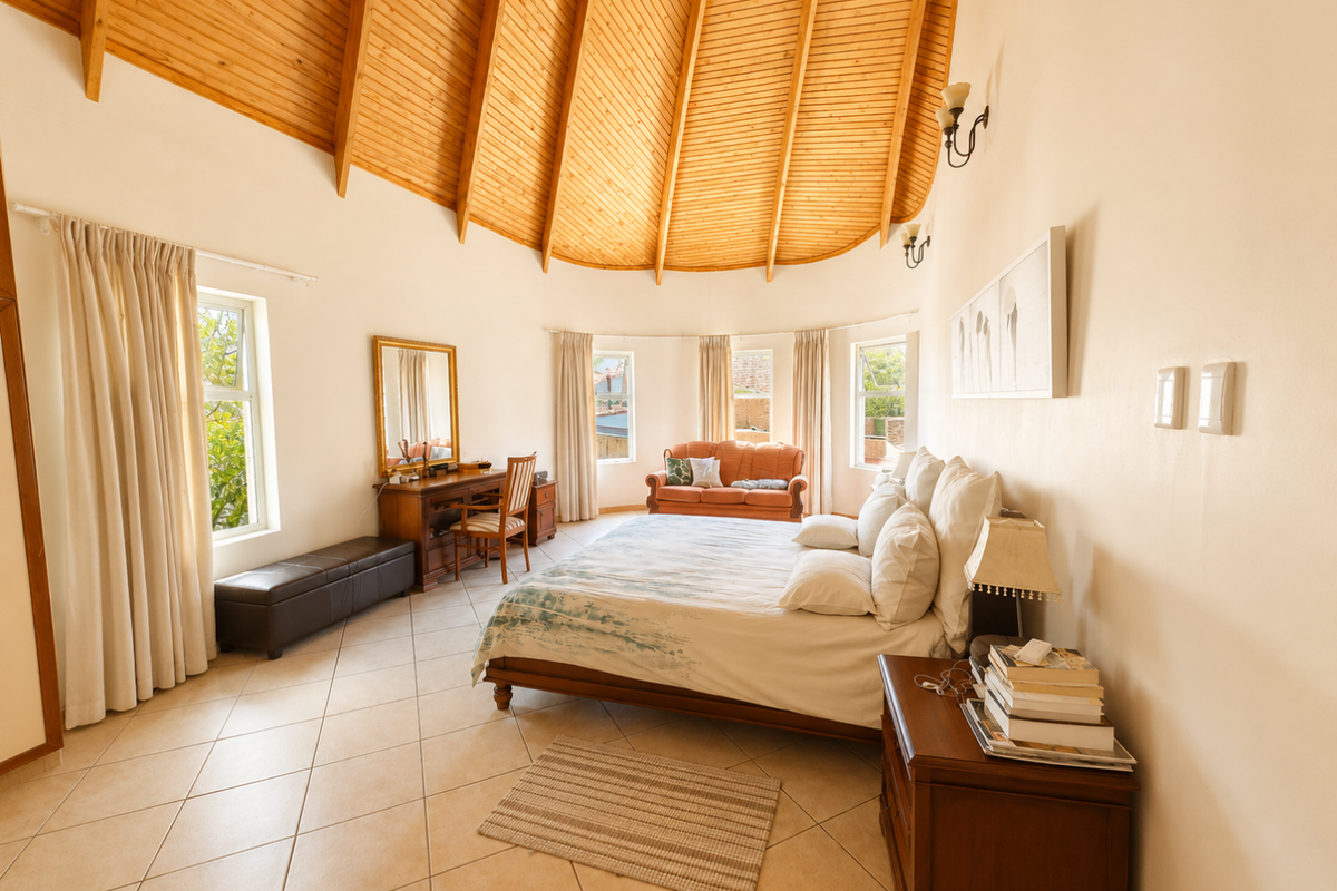Spacious bedroom featuring a high vaulted timber-clad ceiling, tiled flooring, and multiple windows providing natural light.