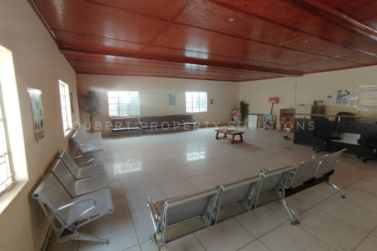 Spacious commercial waiting area featuring tiled flooring, large windows for natural light, and a wood-paneled ceiling.