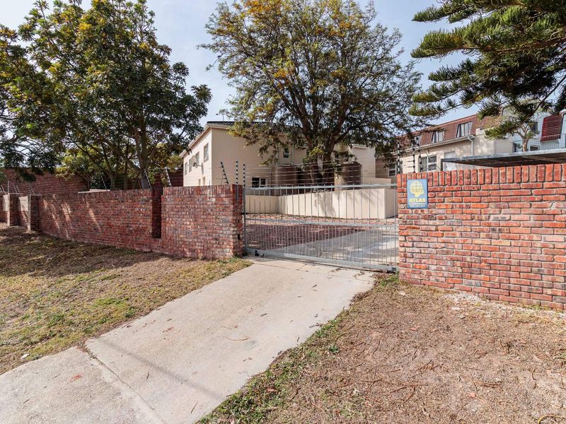 Front exterior view featuring a brick boundary wall with electric fencing, a metal driveway gate, and concrete driveway access.