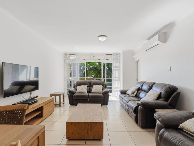 A bright and spacious living room featuring tiled flooring, a wall-mounted air conditioning unit, and direct access to a balcony through sliding glass doors.