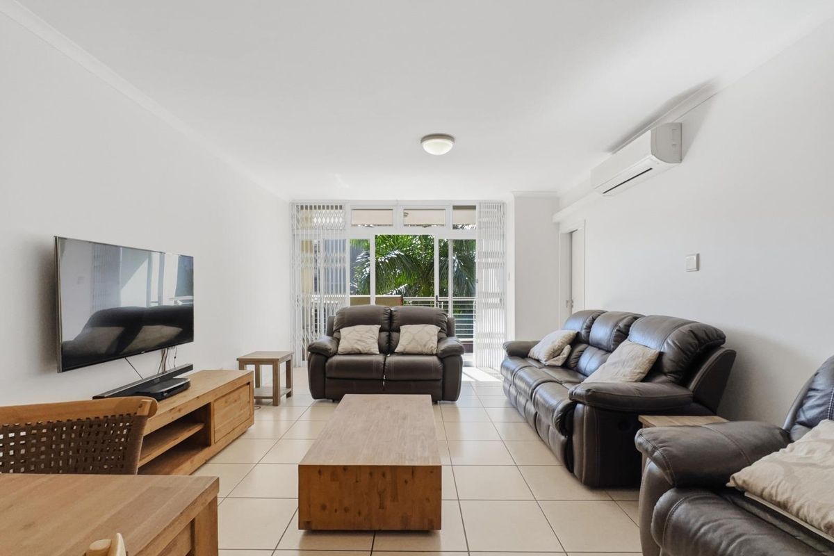 A bright and spacious living room featuring tiled flooring, a wall-mounted air conditioning unit, and direct access to a balcony through sliding glass doors.