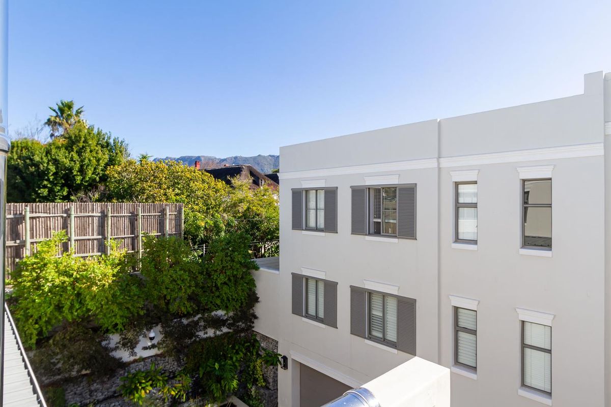 A view of the rear elevation of the townhouse, featuring a clean plastered facade, grey shutters, and established garden greenery.