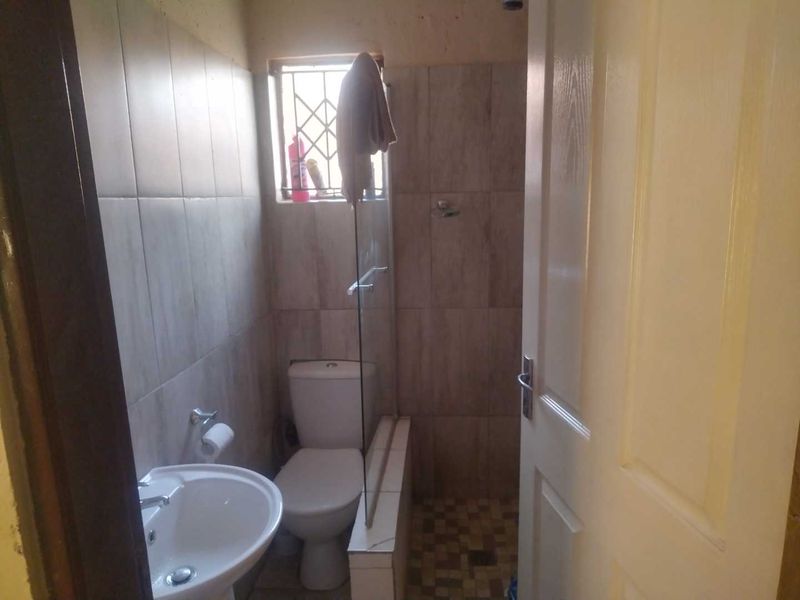 A compact bathroom featuring a pedestal basin, toilet, and a shower enclosure with tiled walls and flooring.