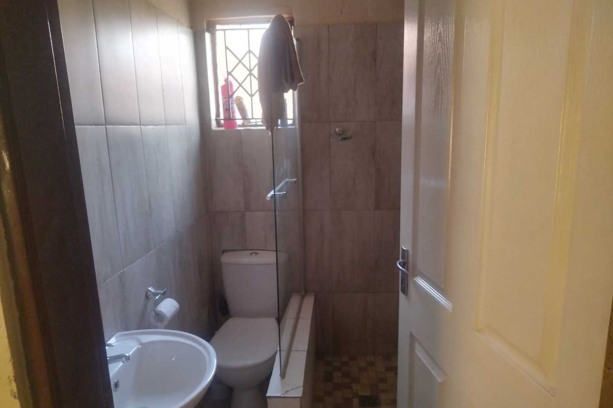 A compact bathroom featuring a pedestal basin, toilet, and a shower enclosure with tiled walls and flooring.