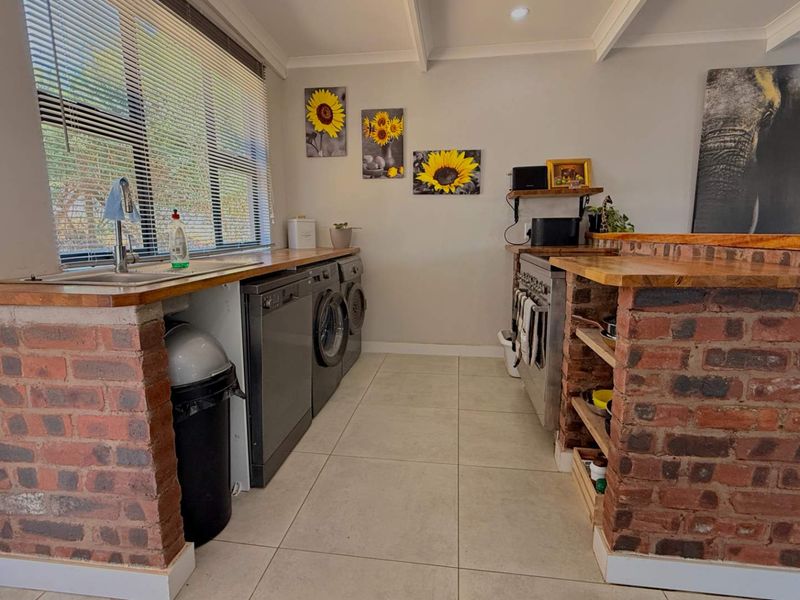 A functional laundry area featuring exposed brick cabinetry, wooden countertops, a stainless steel sink, and tiled flooring with integrated appliance spaces.