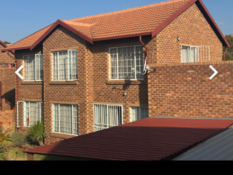 A view of the rear exterior of a double-story face-brick apartment building featuring a tiled roof and security bars on the windows.