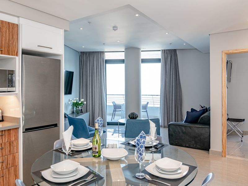 Modern open-plan living and dining area featuring a sleek kitchen with built-in appliances, tiled floors, and direct access to a private balcony.