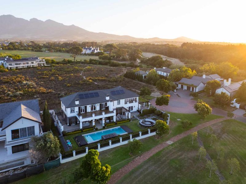 Aerial view of a luxury residence featuring a swimming pool, solar panels, and landscaped grounds in a scenic estate setting.