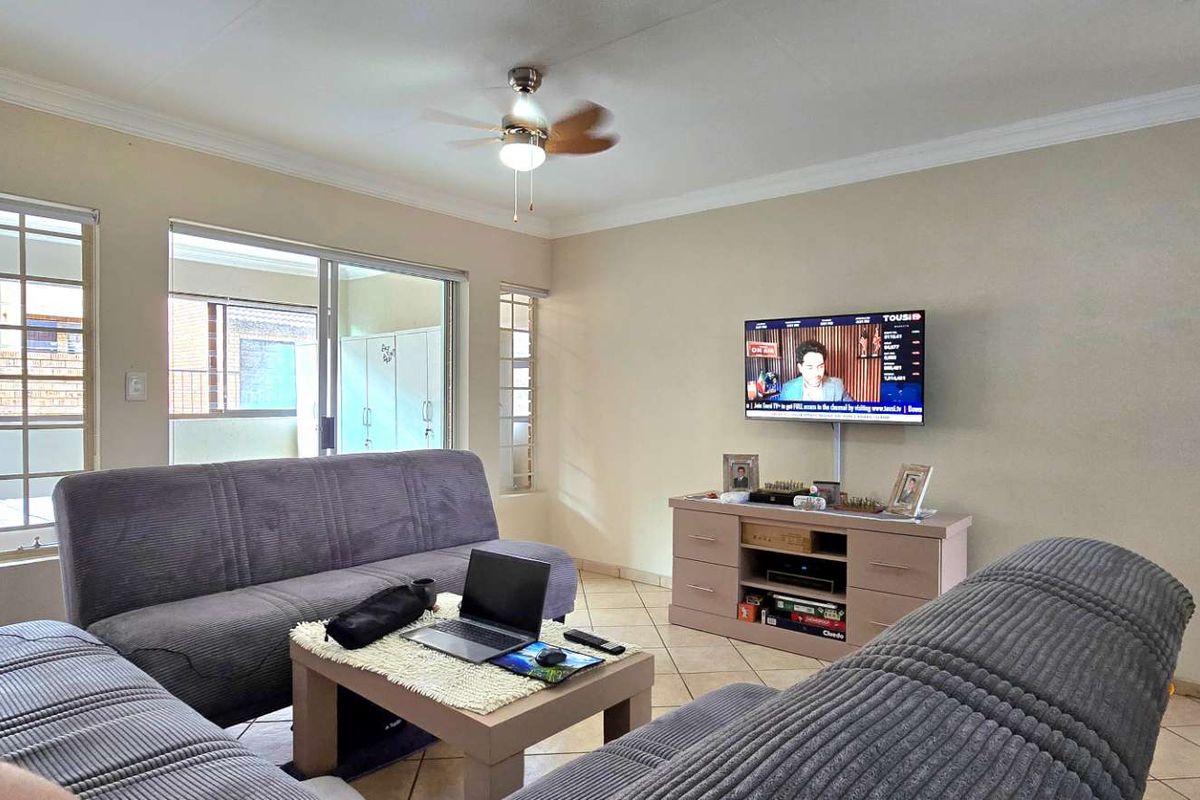 A comfortable living room featuring tiled flooring, a ceiling fan, and large windows providing natural light with access to an outdoor area.
