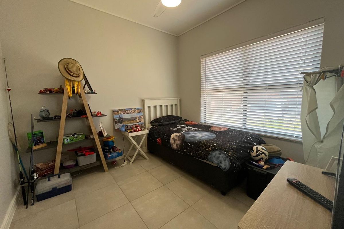 A functional bedroom featuring neutral tiled flooring, a ceiling fan, and large windows fitted with venetian blinds for adjustable natural light.