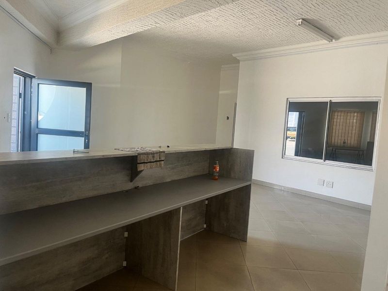 An open-plan interior space featuring tiled flooring, a built-in counter, and a textured ceiling, suitable for a variety of commercial or residential uses.