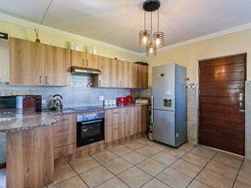 A functional kitchen featuring wood-finish cabinetry, granite countertops, built-in oven, extractor fan, and tiled flooring, offering a practical layout for daily cooking.