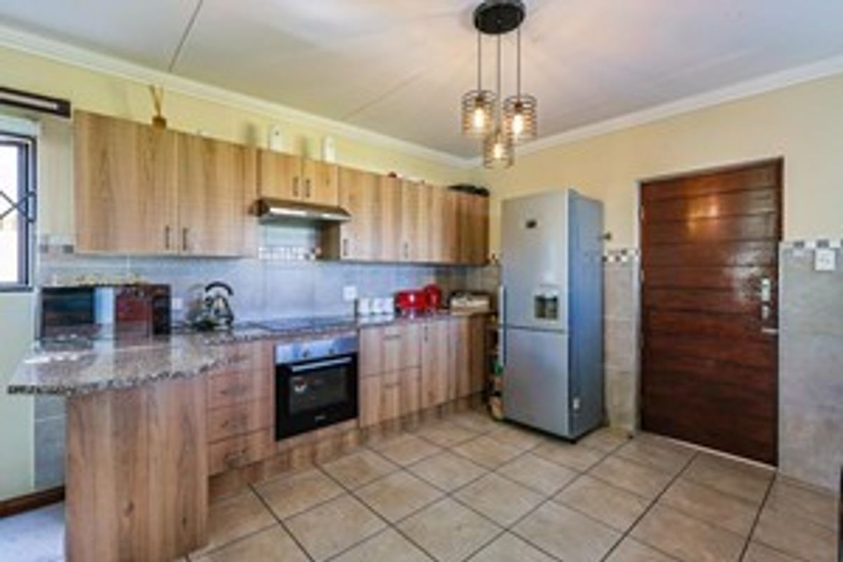 A functional kitchen featuring wood-finish cabinetry, granite countertops, built-in oven, extractor fan, and tiled flooring, offering a practical layout for daily cooking.