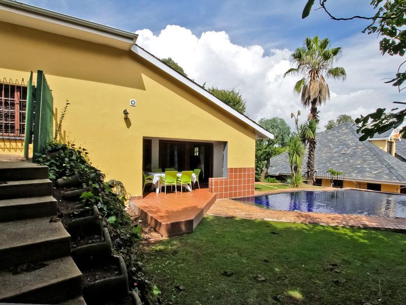 Rear exterior view featuring a swimming pool, tiled patio area, and concrete stairs leading to the garden.