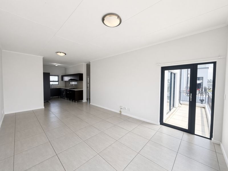 Spacious open-plan living area featuring neutral tiled flooring, a modern kitchen with dark cabinetry, and direct access to a private balcony through glass doors.