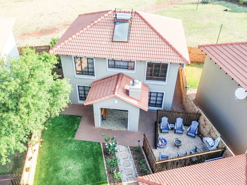Aerial view of a two-story house featuring a terracotta tiled roof with solar heating, a covered patio, and a landscaped garden with paved areas.