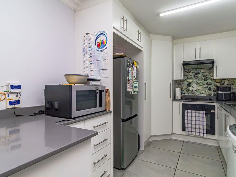 A functional kitchen featuring white cabinetry, stone countertops, built-in oven with extractor fan, and tiled flooring.
