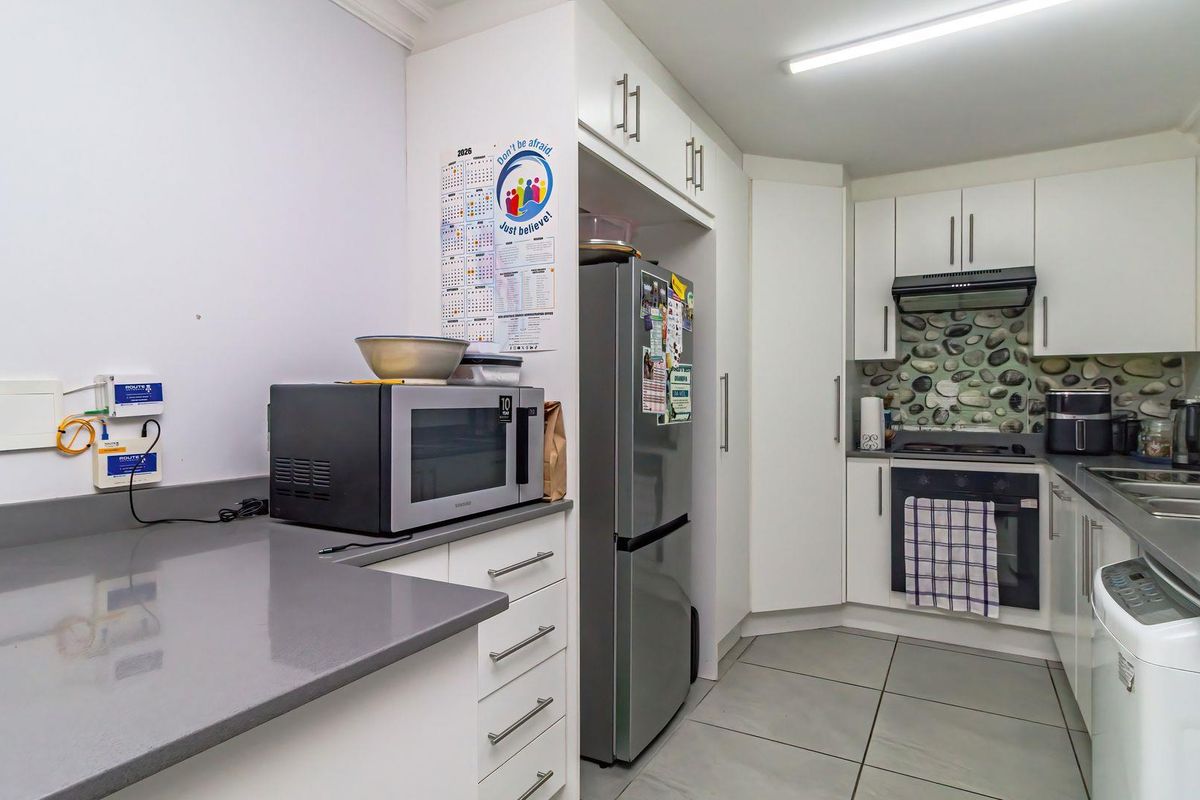 A functional kitchen featuring white cabinetry, stone countertops, built-in oven with extractor fan, and tiled flooring.