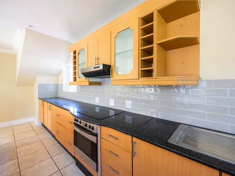 A functional kitchen featuring light wood cabinetry, dark granite countertops, a subway tile backsplash, and integrated cooking appliances.