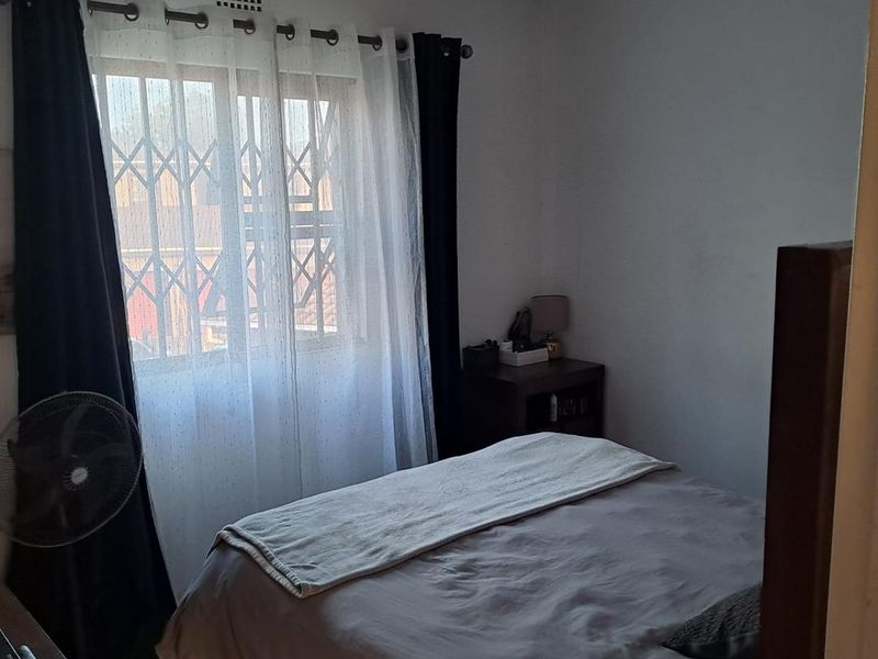 A functional bedroom featuring tiled flooring and a window fitted with a security gate, providing a simple and practical living space.