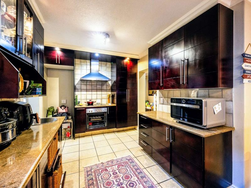 A functional kitchen featuring dark wood cabinetry, granite countertops, a built-in oven with extractor fan, and tiled flooring.