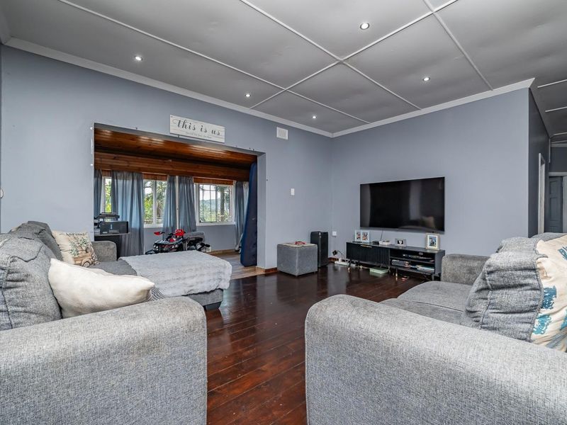 Spacious living room featuring dark timber flooring, recessed downlights, and a tiled ceiling, with an adjoining area visible through the wide opening.