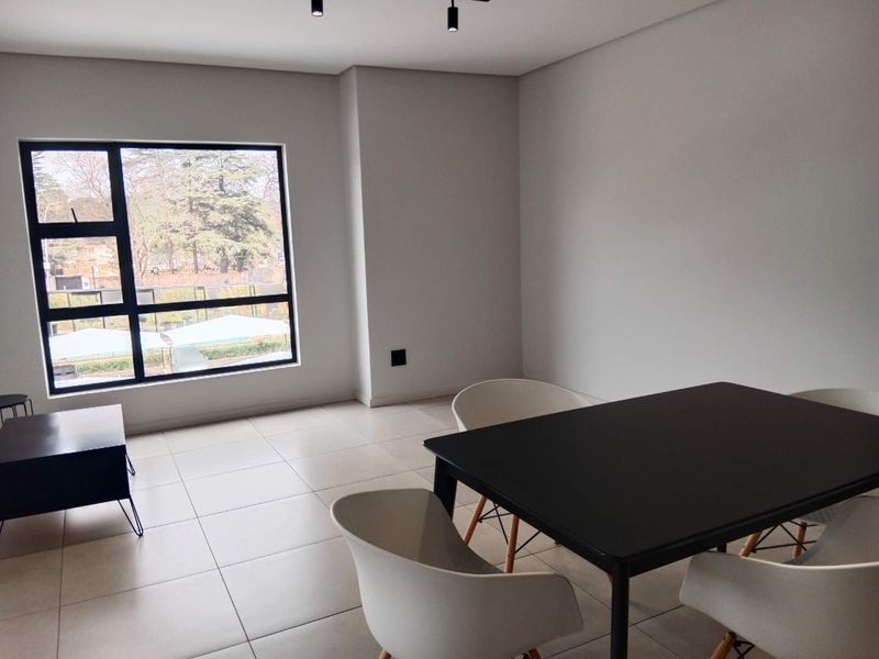 A bright and modern living area featuring large windows, neutral tiled flooring, and contemporary track lighting, offering a clean and versatile space.