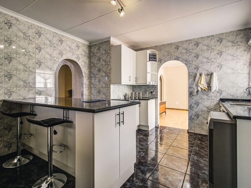 A functional kitchen featuring white cabinetry, granite countertops, a breakfast bar, and distinctive patterned wall tiling with an arched entryway.