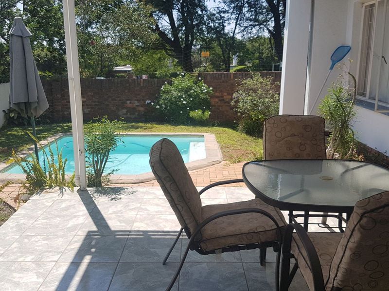 Covered patio area featuring tiled flooring, overlooking a private swimming pool and garden with brick boundary walling.