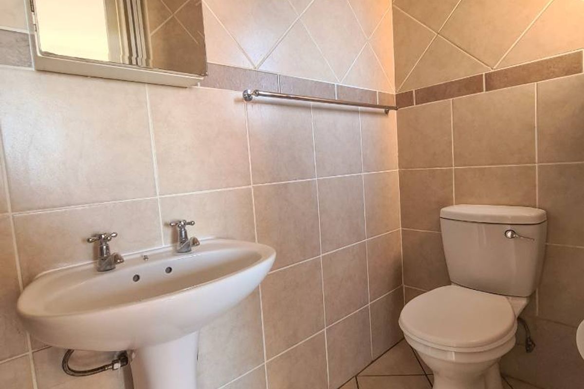 A functional bathroom featuring a pedestal basin, toilet, and neutral wall and floor tiling with a wall-mounted mirror.