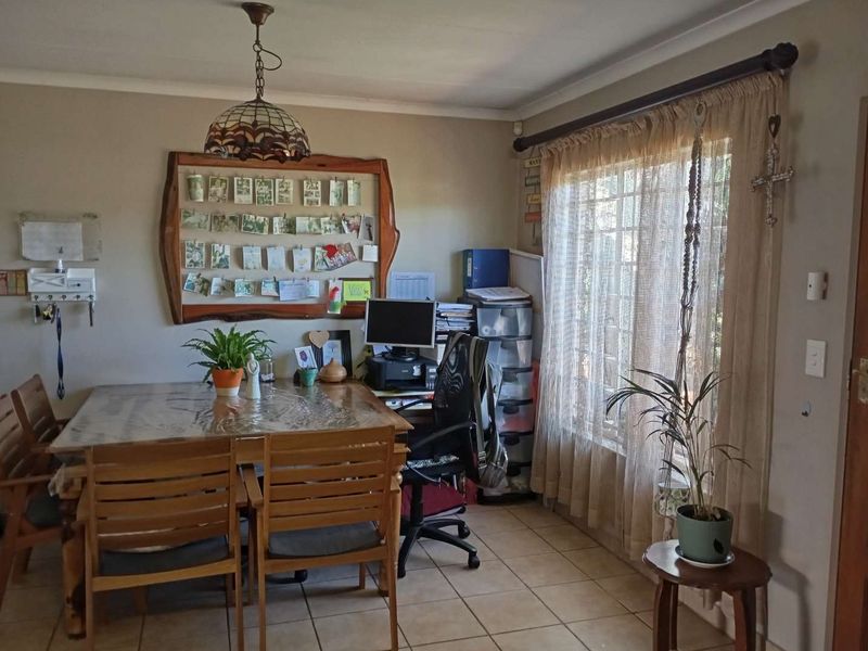 A functional dining area featuring tiled flooring, cove cornicing, and a window fitted with security bars, currently utilized as a multi-purpose space.