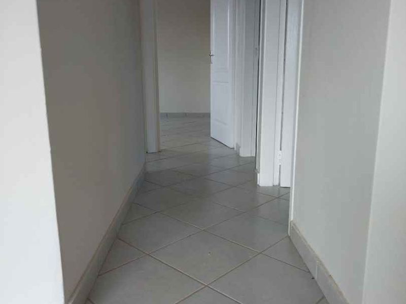 A clean, empty hallway featuring neutral tiled flooring and multiple internal doors leading to adjacent rooms.