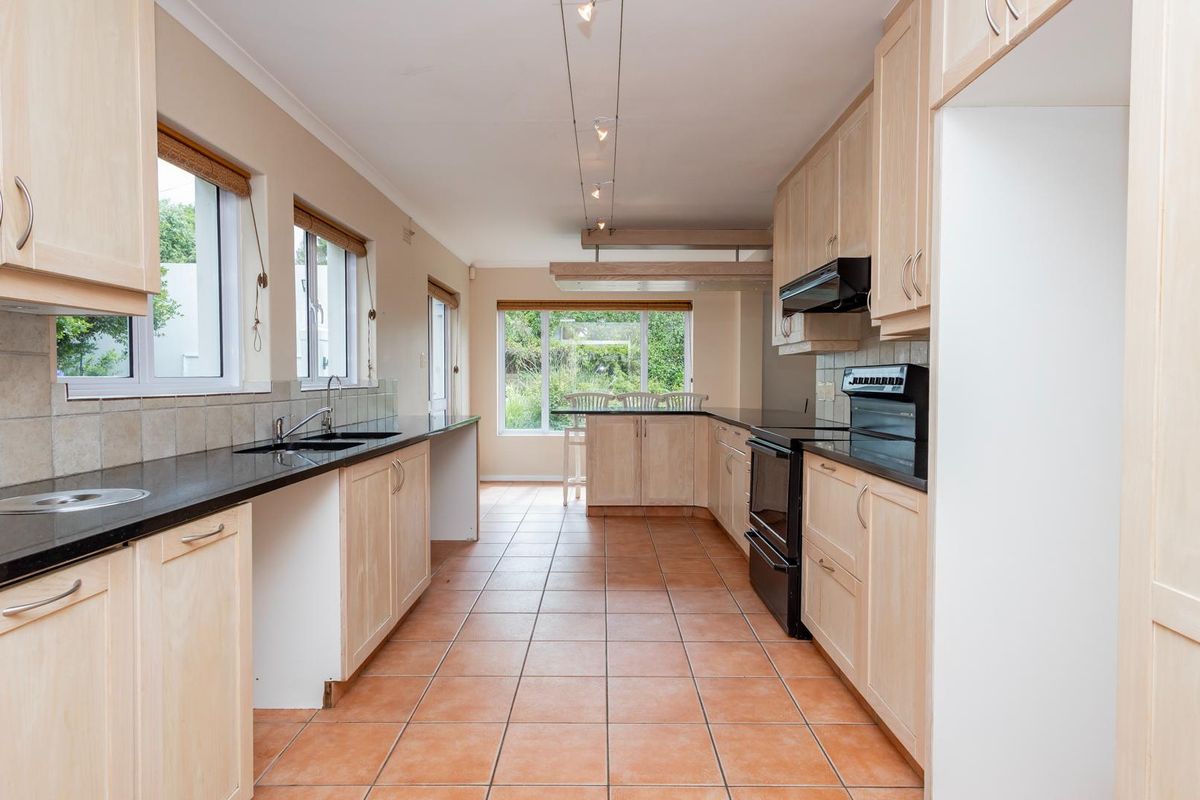 Spacious kitchen featuring light-wood cabinetry, black granite countertops, tiled flooring, and ample natural light from multiple windows.