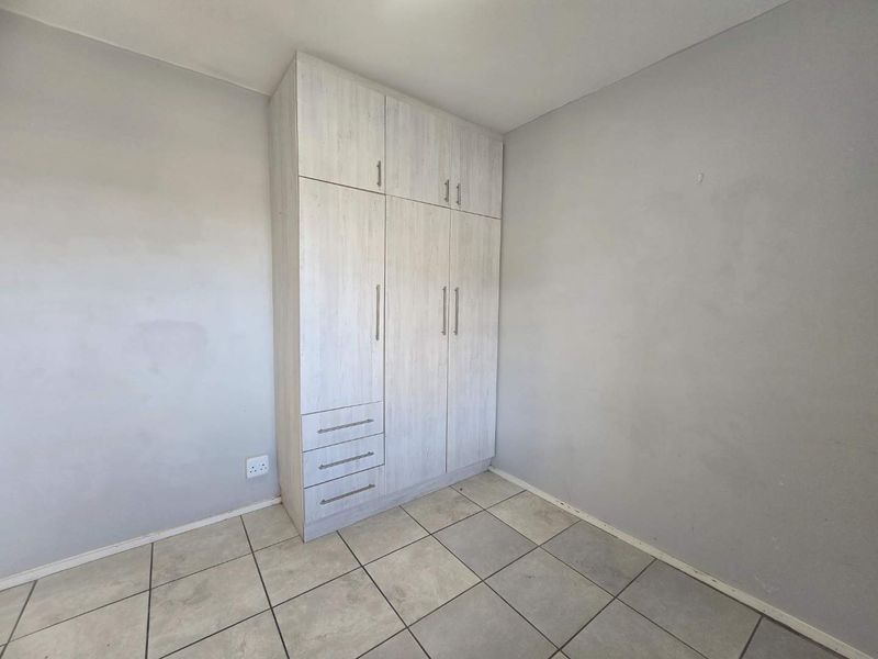 A vacant bedroom featuring light-toned built-in cabinetry with integrated drawers and neutral tiled flooring.