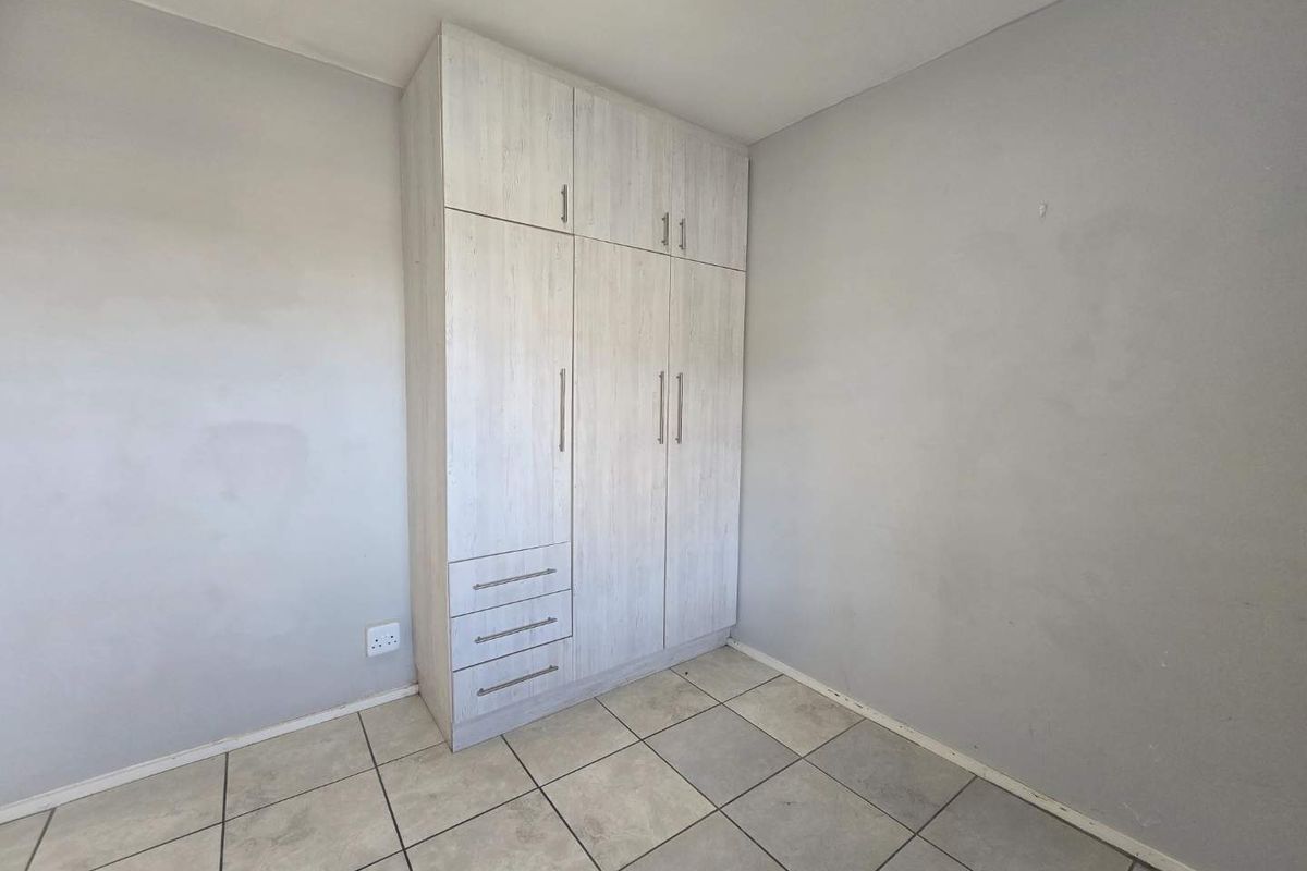 A vacant bedroom featuring light-toned built-in cabinetry with integrated drawers and neutral tiled flooring.